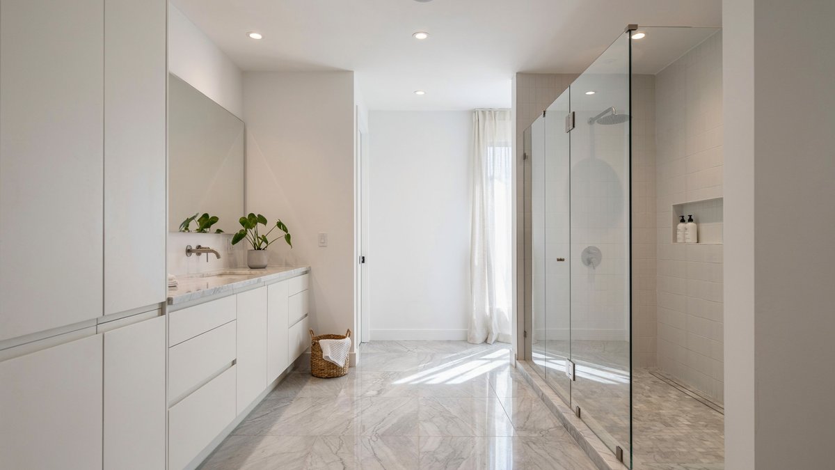 Bright white master bath with a frameless glass shower and marble floor