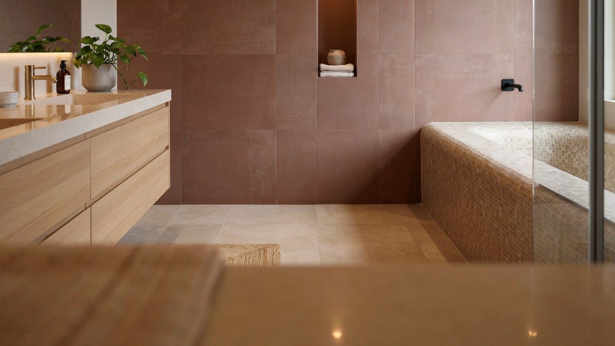 Sleek brown bathroom with a mosaic-clad tub and cream quartzite vanity counter