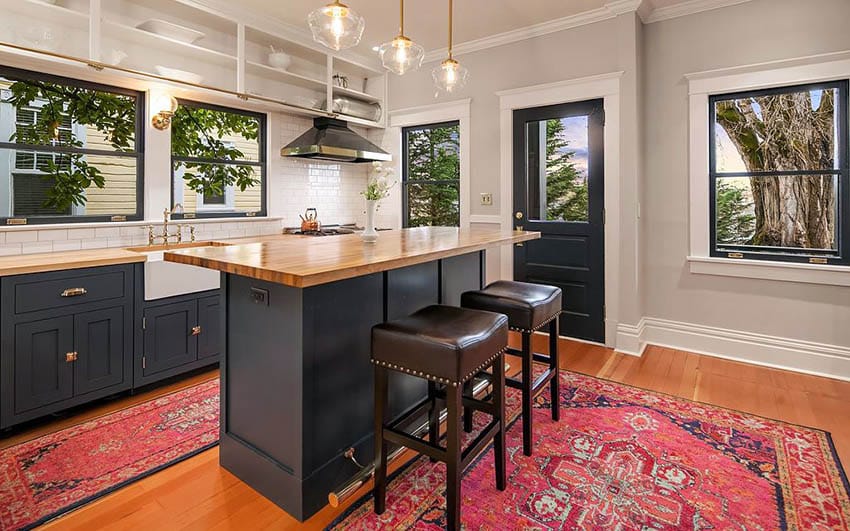 Small open plan kitchen with wood countertop island, dark gray cabinets, white subway tile backsplash and wood flooring