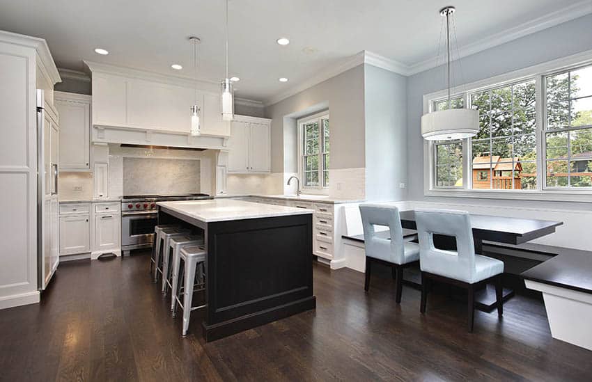 Kitchen with walls in white finish, drum chandelier and stools under dark painted island