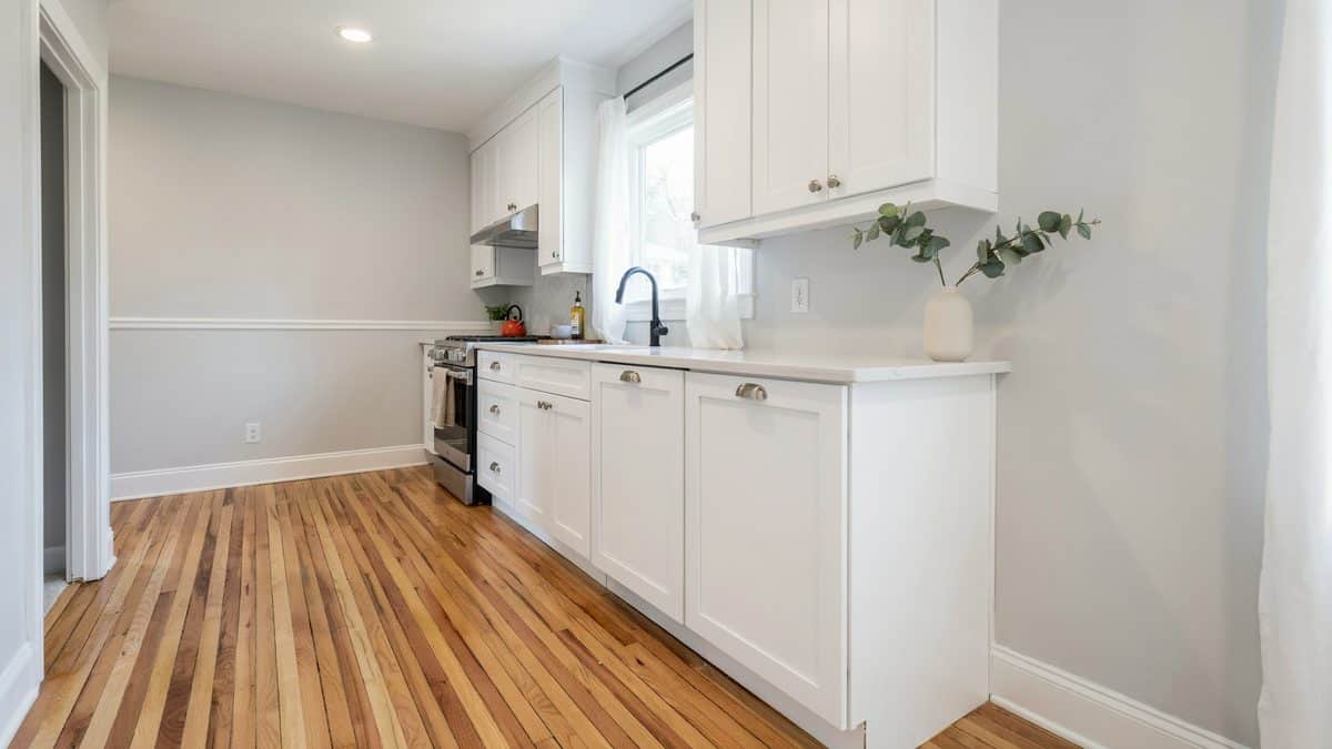 White shaker galley kitchen with quartz counters and raw honey plank floors