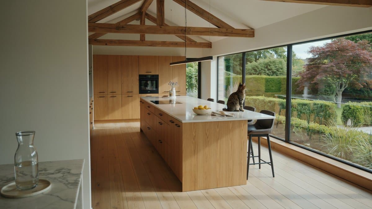 Oak kitchen with exposed ceiling trusses and white island beside garden windows