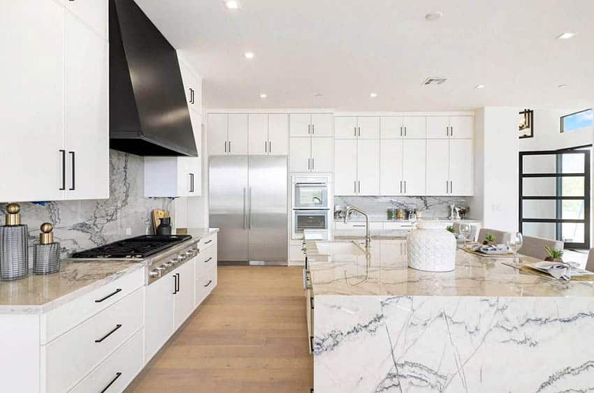 stylish kitchen with white flat panel cabinets, black oven hood and waterfall quartz tops