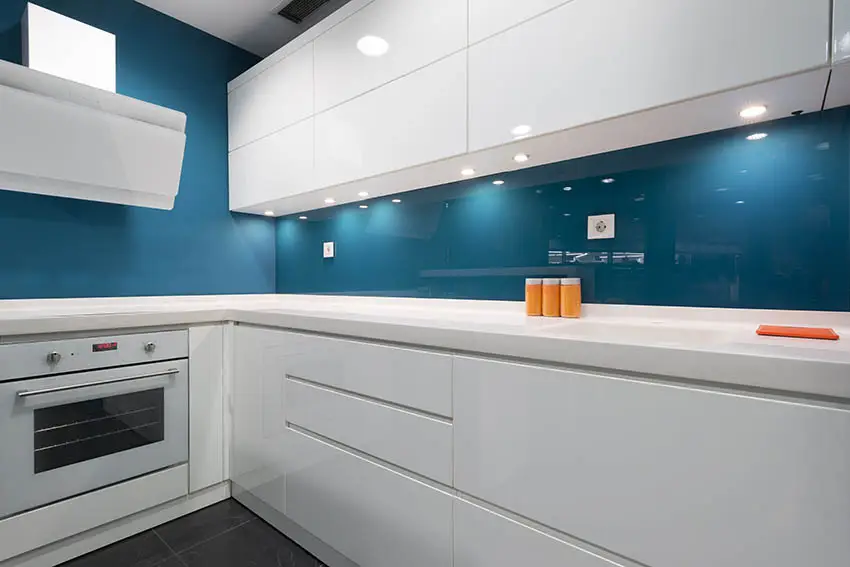 L shaped modern kitchen with white cabinets and dark blue glass backsplash