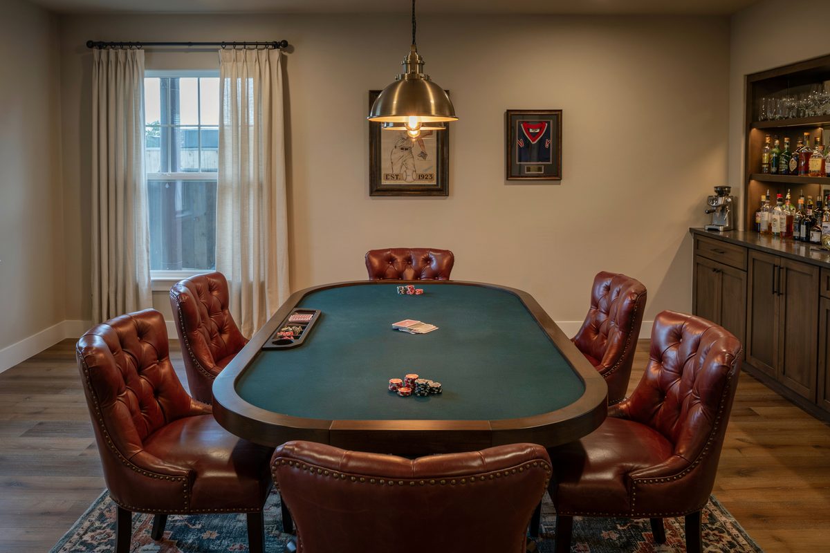 Light brown poker room with tufted leather chairs and brass pendant light