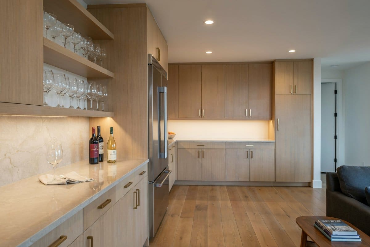 Light beech lower level bar with beige granite counter and wine glass shelves