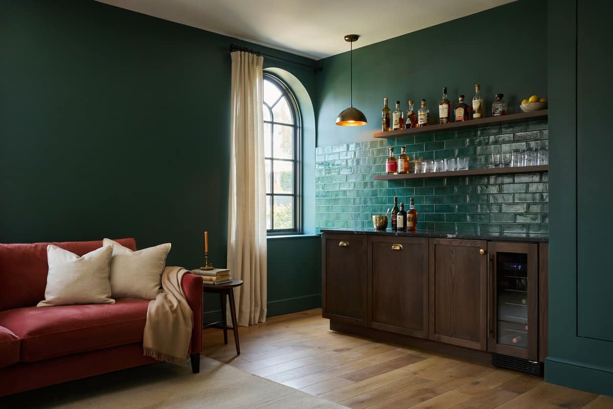 Dark walnut home bar with emerald green tile backsplash and red velvet sofa