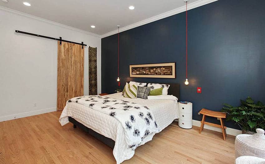 Bedroom with sliding barn door, white bed and wood flooring