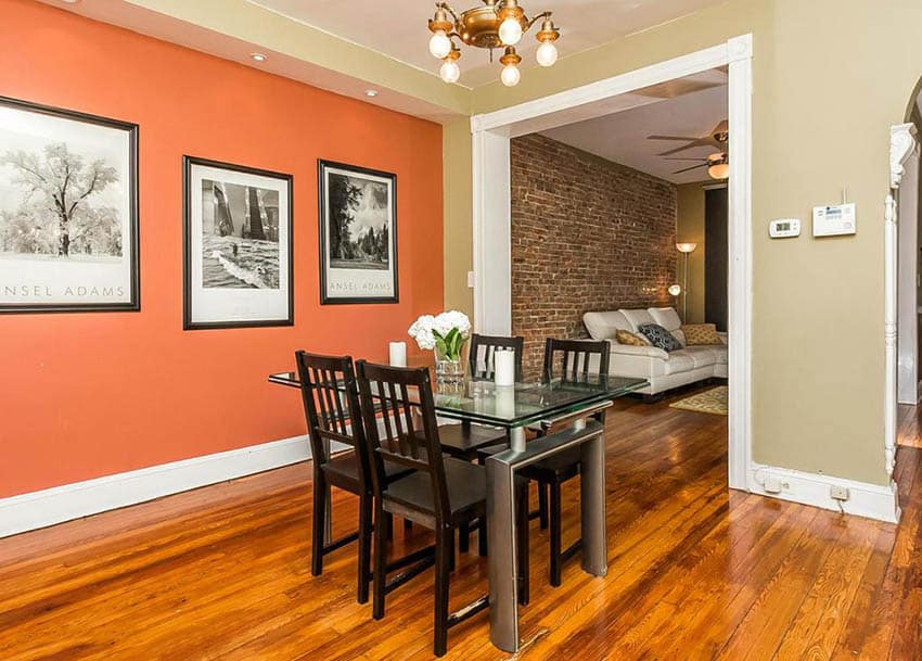 Tan dining room with bright orange accent wall and wood flooring