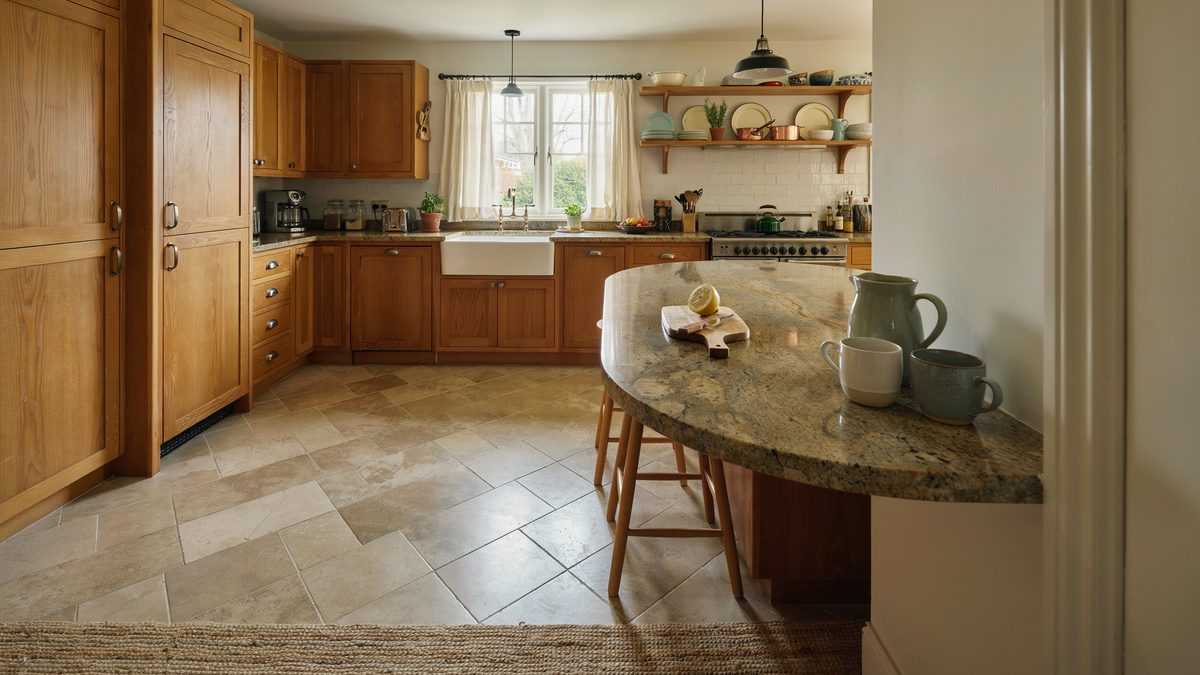 Honey oak cabinetry wraps a curved granite breakfast table on travertine tile