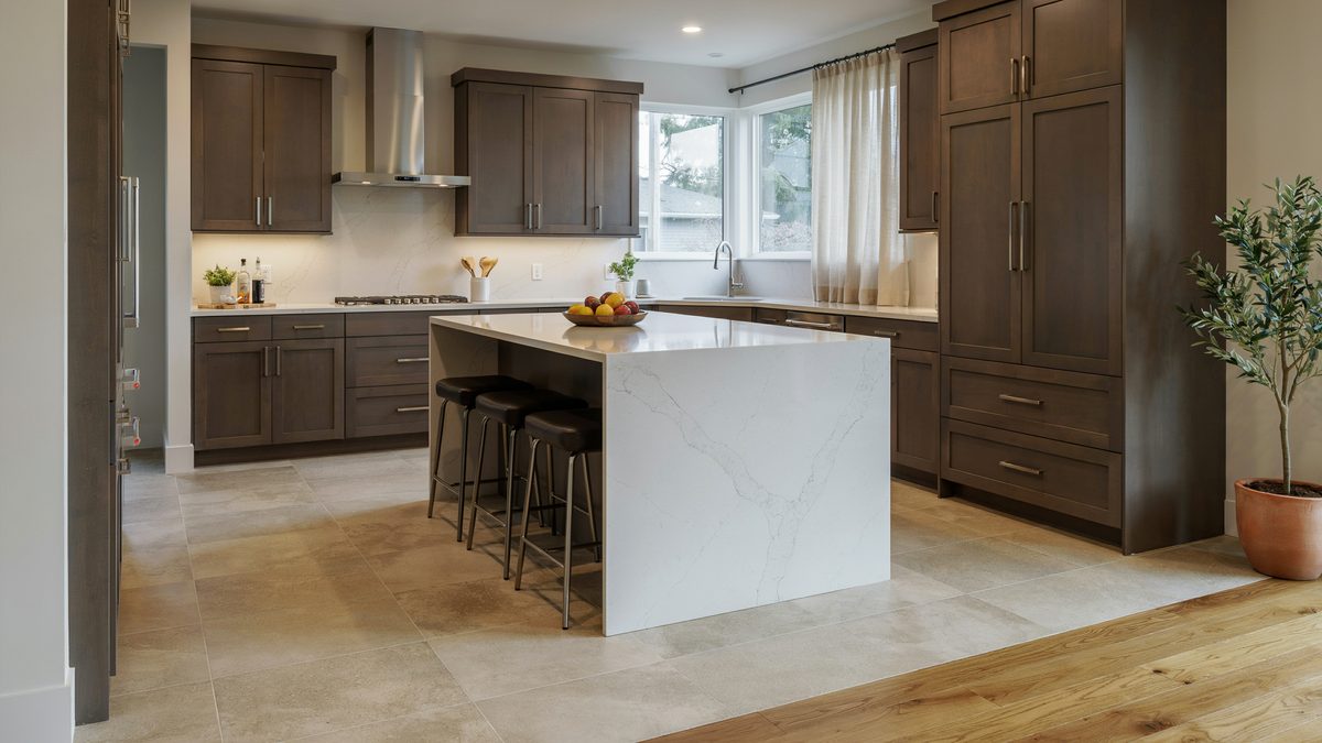 Beige ceramic tile floor in a kitchen with dark brown cabinets and marble island