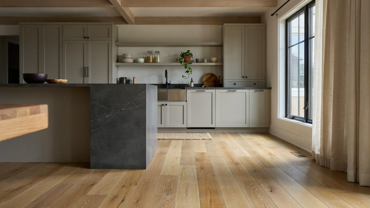 Hickory plank flooring running through a kitchen with soapstone island and wood beams