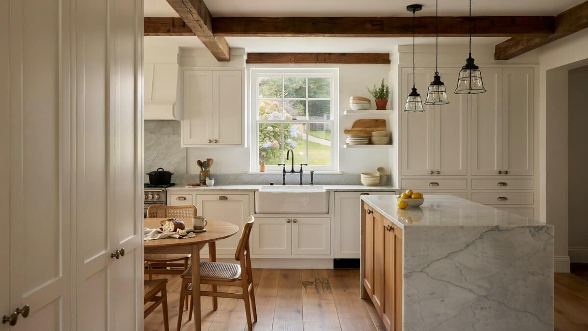 Marble topped island under dark exposed beams with a round dining table alongside