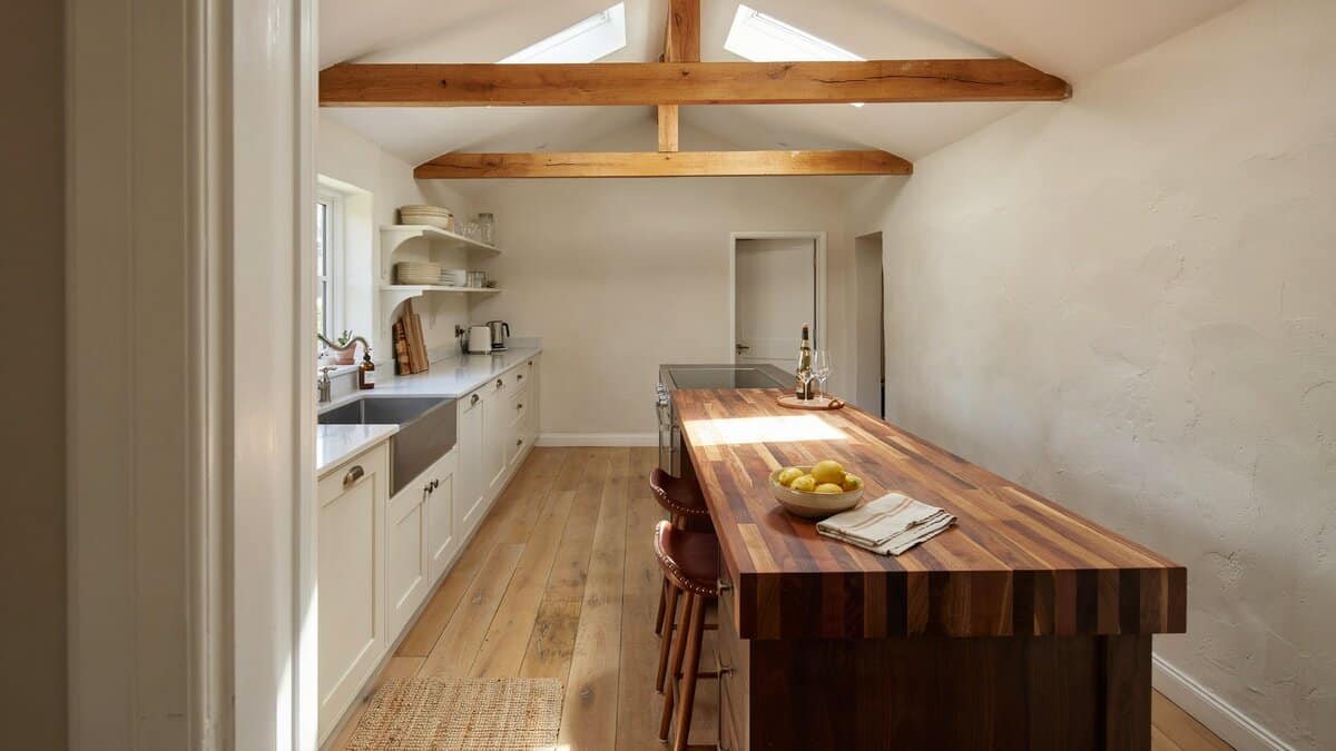 Vaulted white kitchen with a wood truss and long walnut butcher block island
