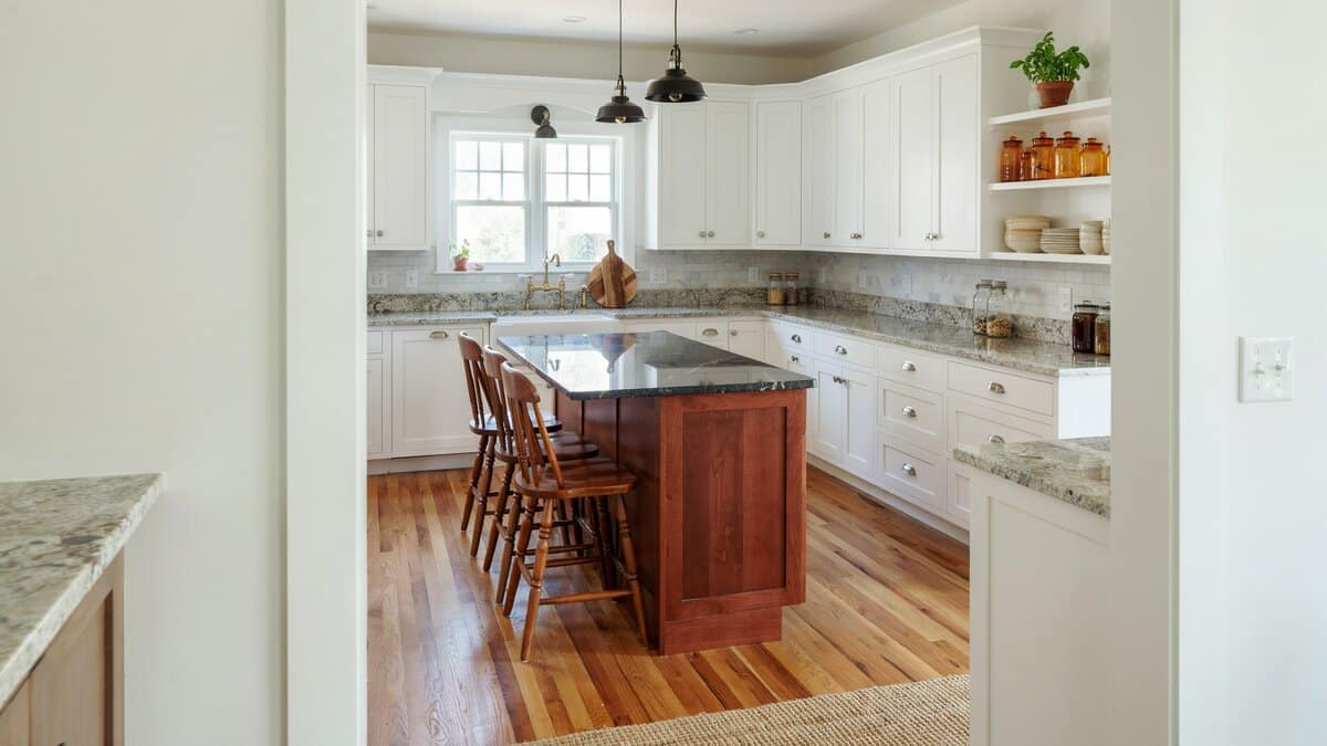 Cherry wood island with a dark top and spindle back stools in a white kitchen