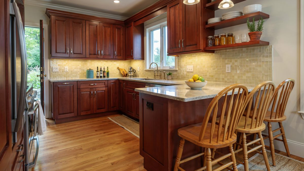 Cherry kitchen with peninsula seating spindle back chairs and tan tile backsplash