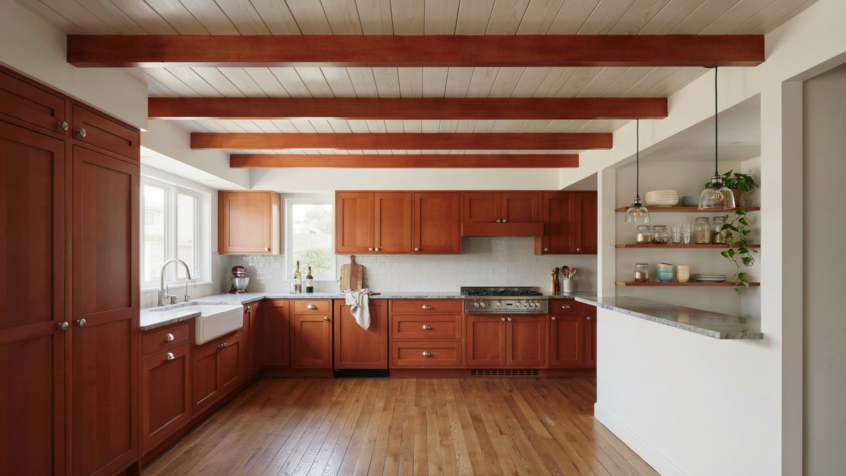 Cherry cabinets under whitewashed plank ceiling with exposed beams and farmhouse sink