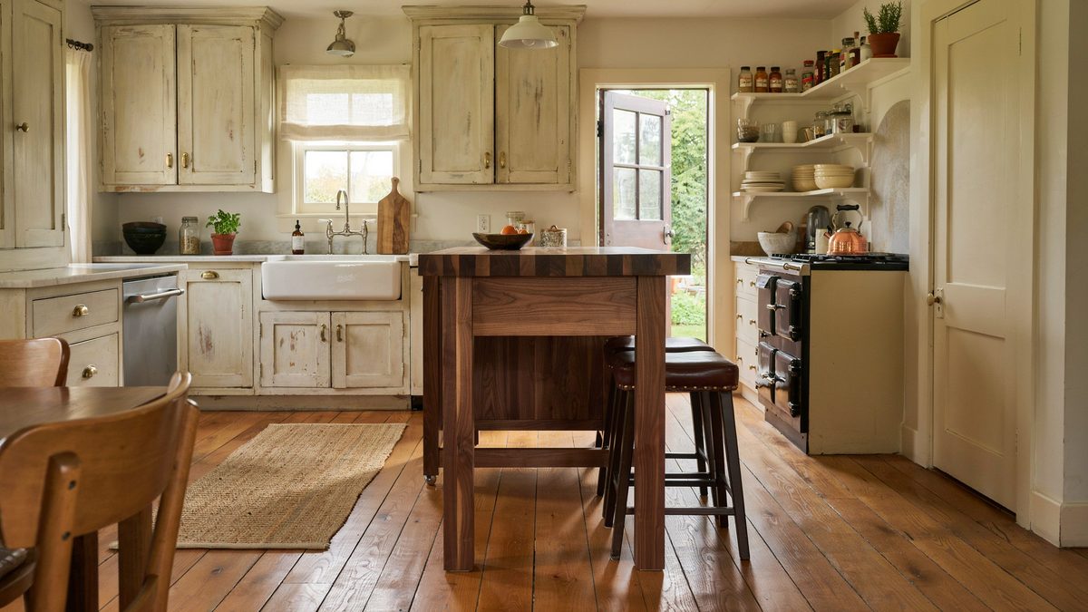 Pale distressed cabinets frame a walnut island beside an open garden door