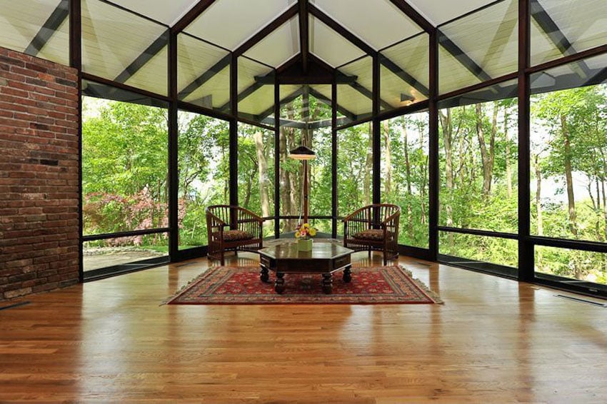 Living room with wraparound windows with tree landscape wood flooring and brick walls