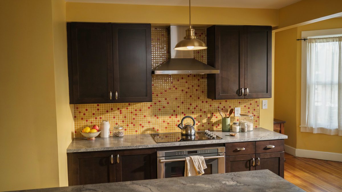 Dark cherry cabinets against golden yellow walls with gold and red mosaic tile