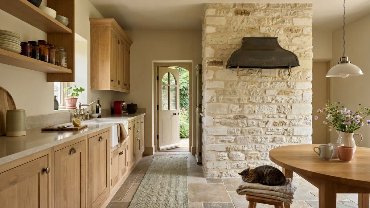 Limestone chimney breast with a black hood beside pale oak cabinets and stone floor