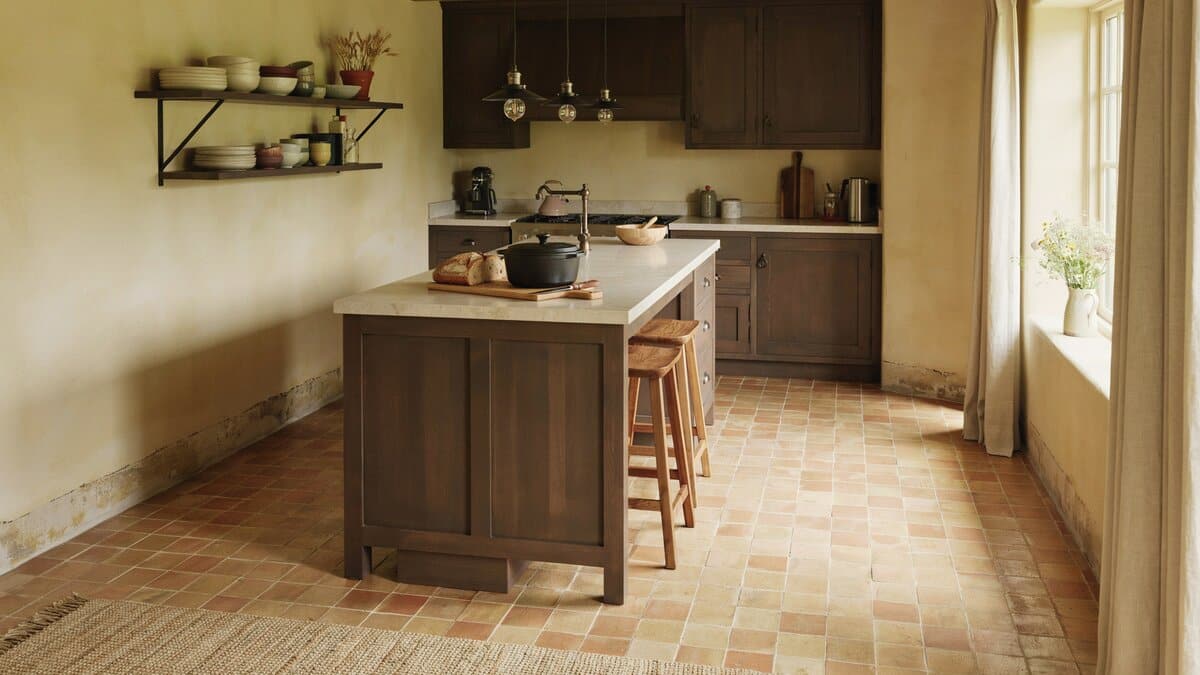 Walnut cabinets and a light topped island above warm orange terracotta floor tiles