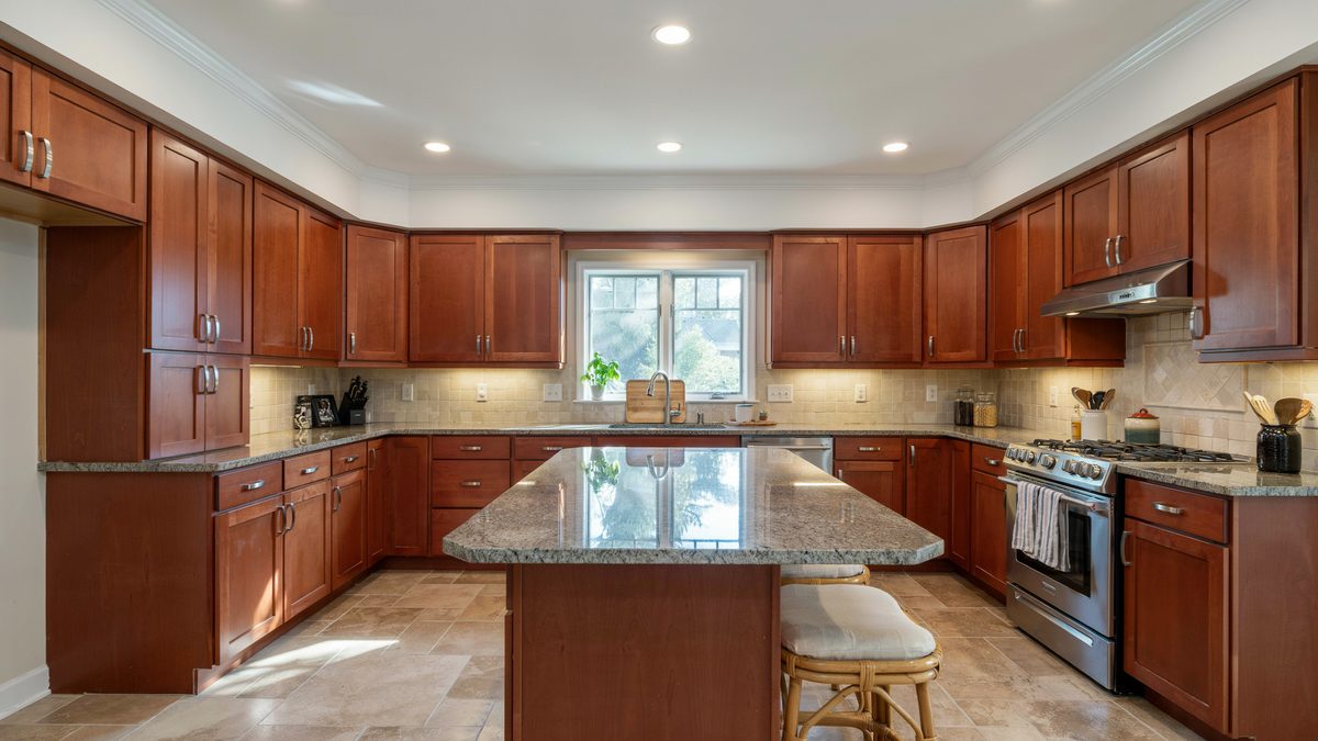 Cherry kitchen with speckled granite island rattan stools and recessed ceiling lights
