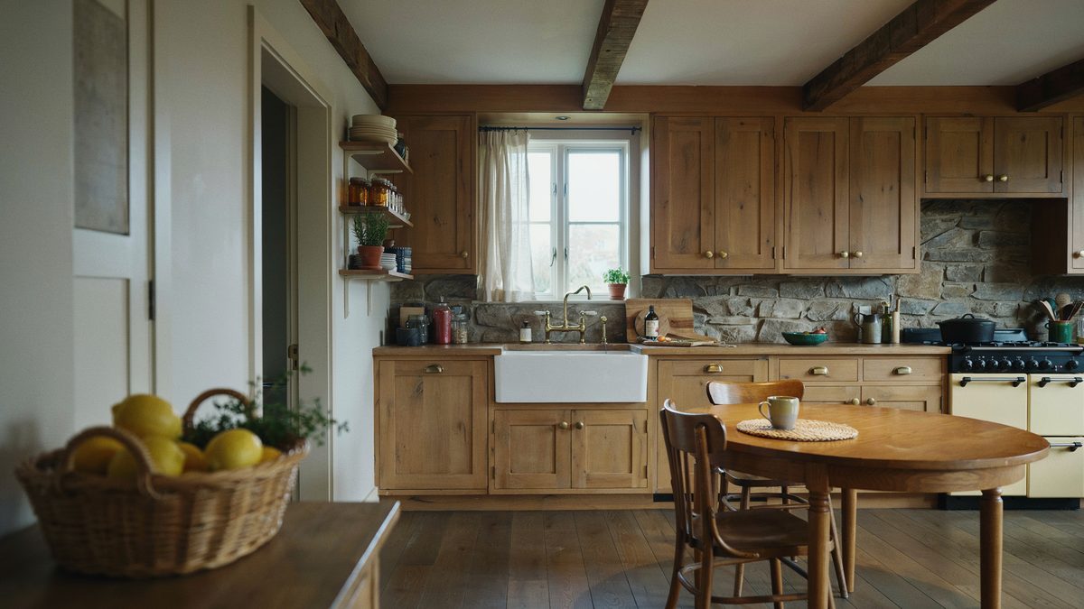 Oak cabinets and beamed ceiling surround a farmhouse sink and slate backsplash