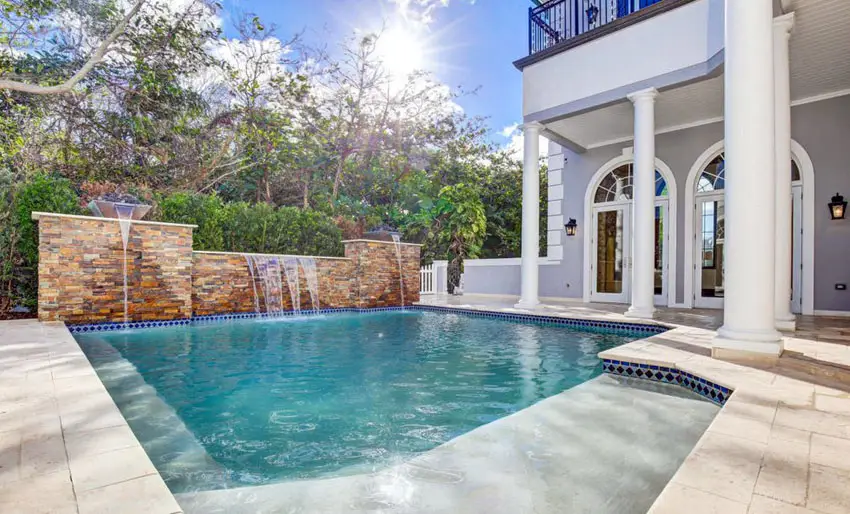 Pool with vase fountain, stone wall and house with white columns