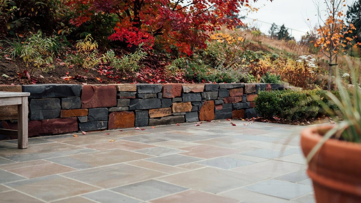 Multicolor stacked stone retaining wall above bluestone paving and autumn shrubs