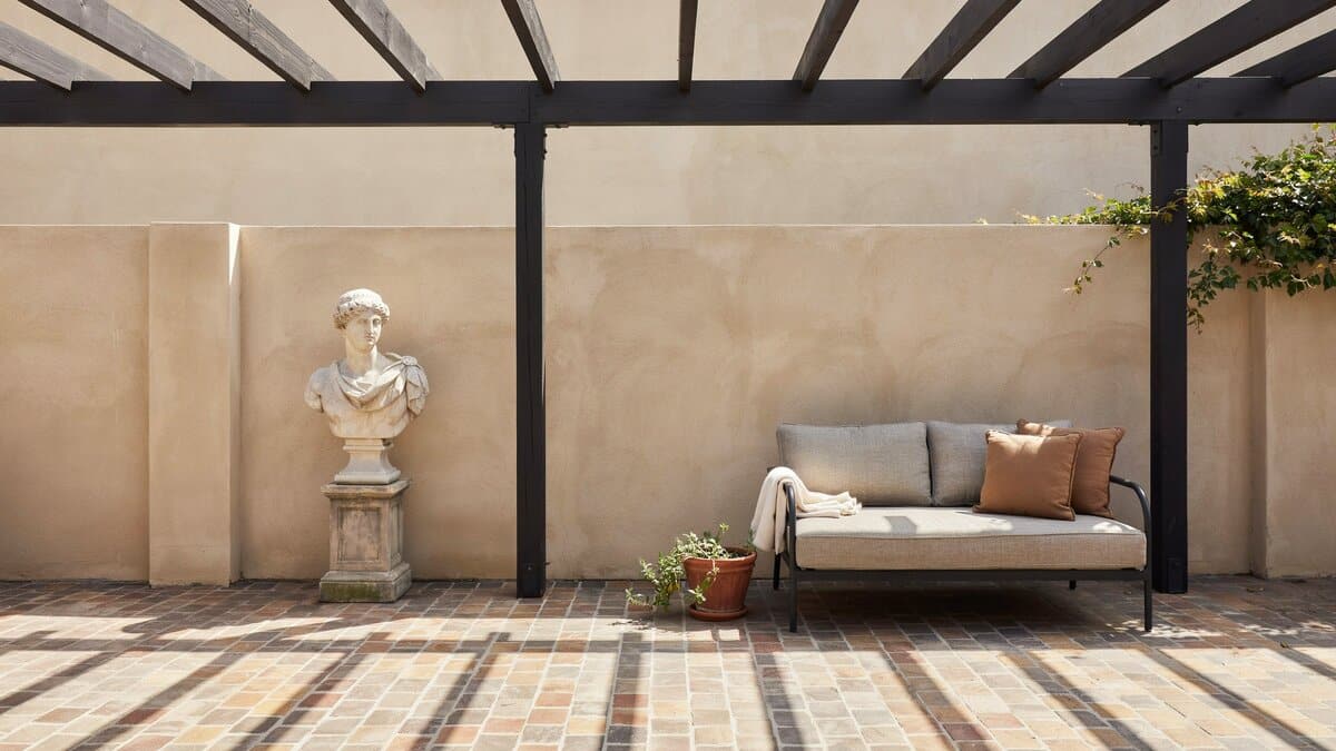 Black pergola over slate paving with a daybed and stone bust statue