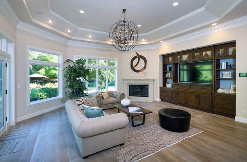 Family room with built in entertainment center, wood floors, tray ceiling, fireplace and tufted couches