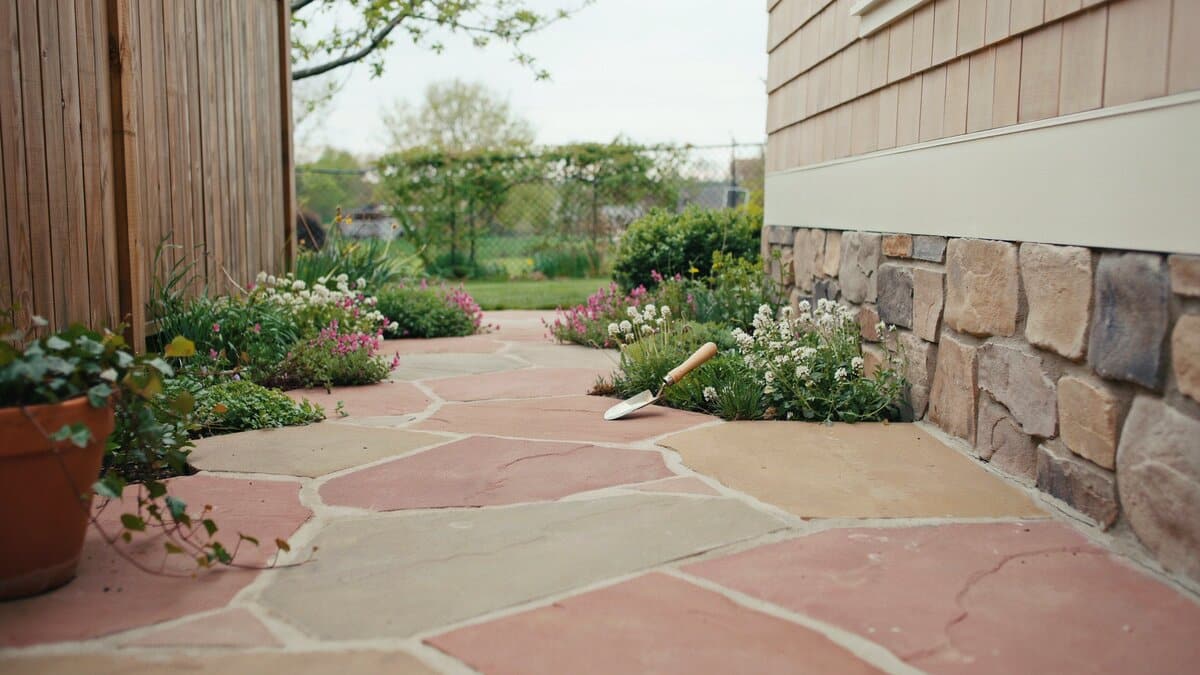Reddish flagstone walkway beside a stone veneer cottage wall and garden beds