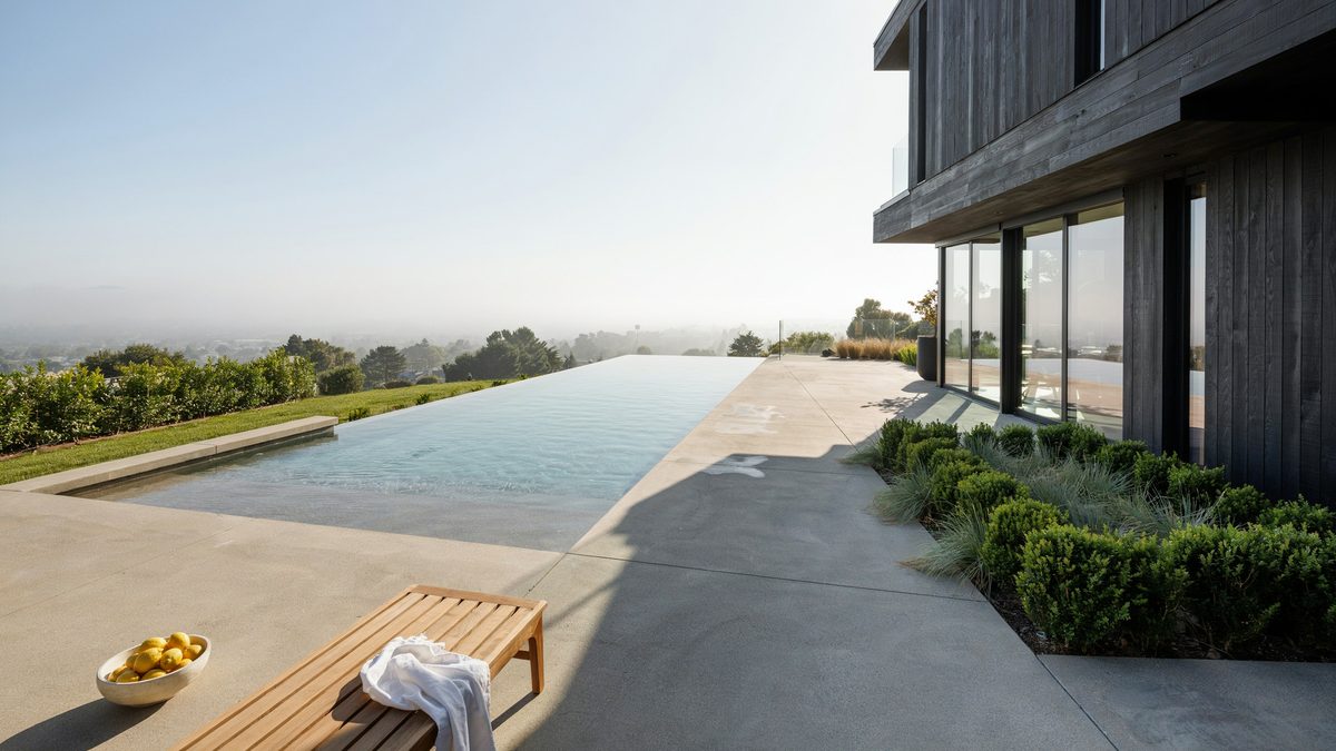 Rectangular vanishing edge pool running alongside a dark modern hillside home