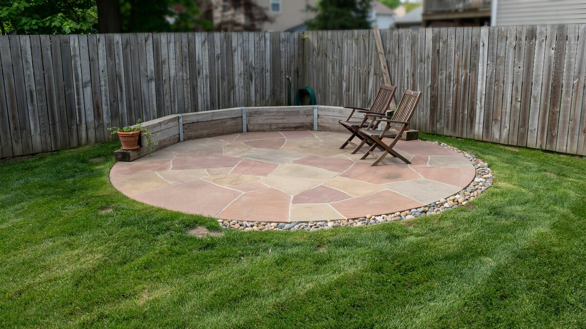 Circular flagstone pad edged with pebbles against a weathered wood fence
