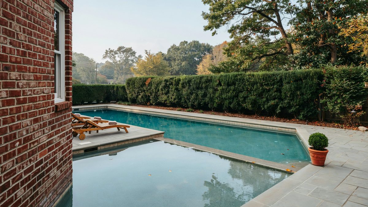 Angled lazy L pool tucked against a red brick house and hedge