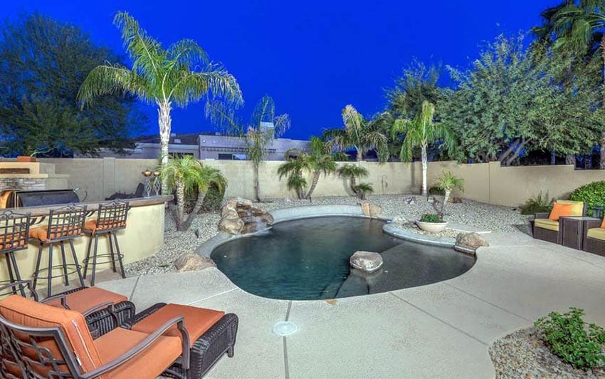 Oasis swimming pool with rock islands next to outdoor kitchen and tropical landscaping