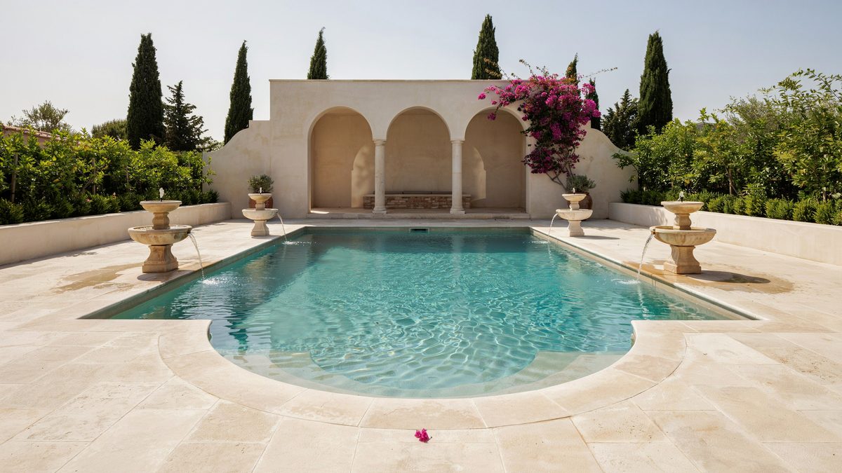 Grecian pool with cut corners facing a stucco cabana with arched openings