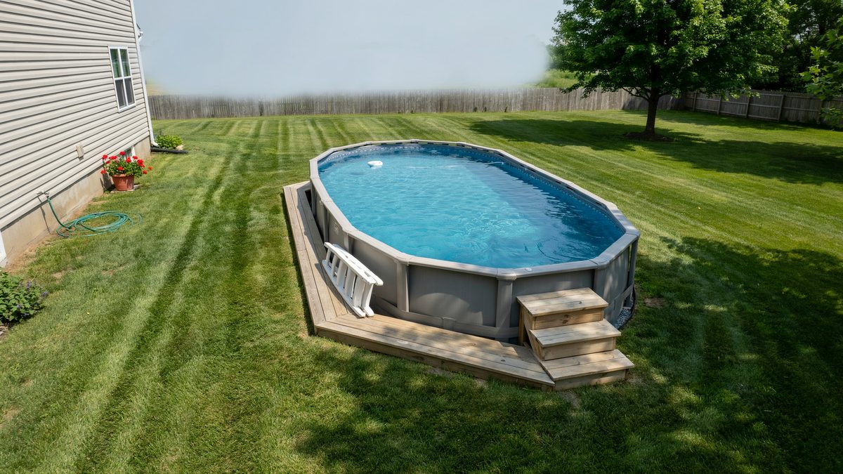 Above ground oval pool with wood step deck on a green lawn