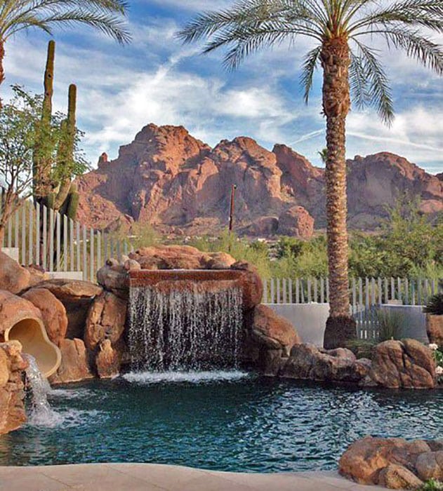 Rock waterfall pool with tunnel slide, palm trees and mountain view