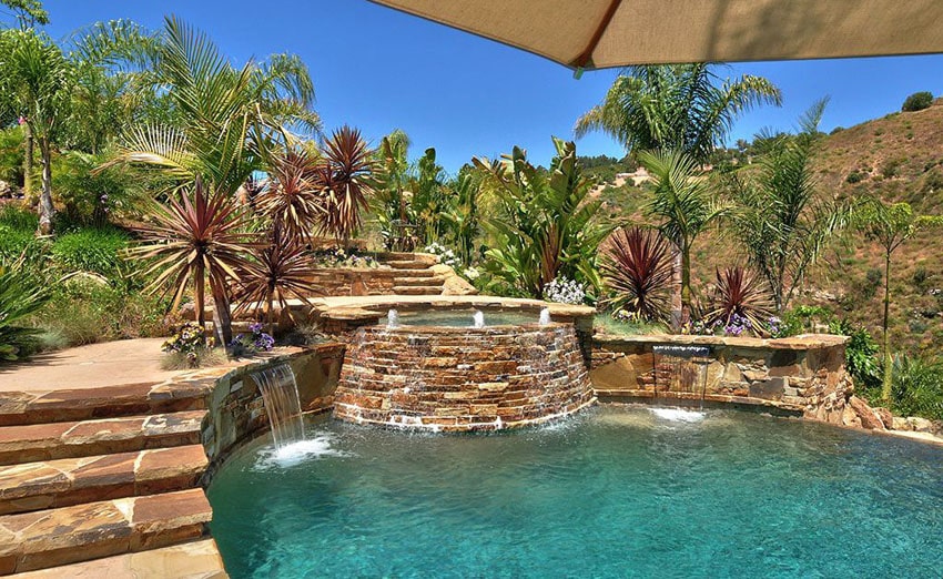 Swimming pool with tropical landscaping and stacked stone spa with waterfalls