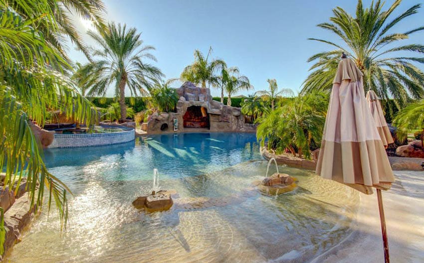 Tropical swimming pool with sand beach entry and sitting grotto