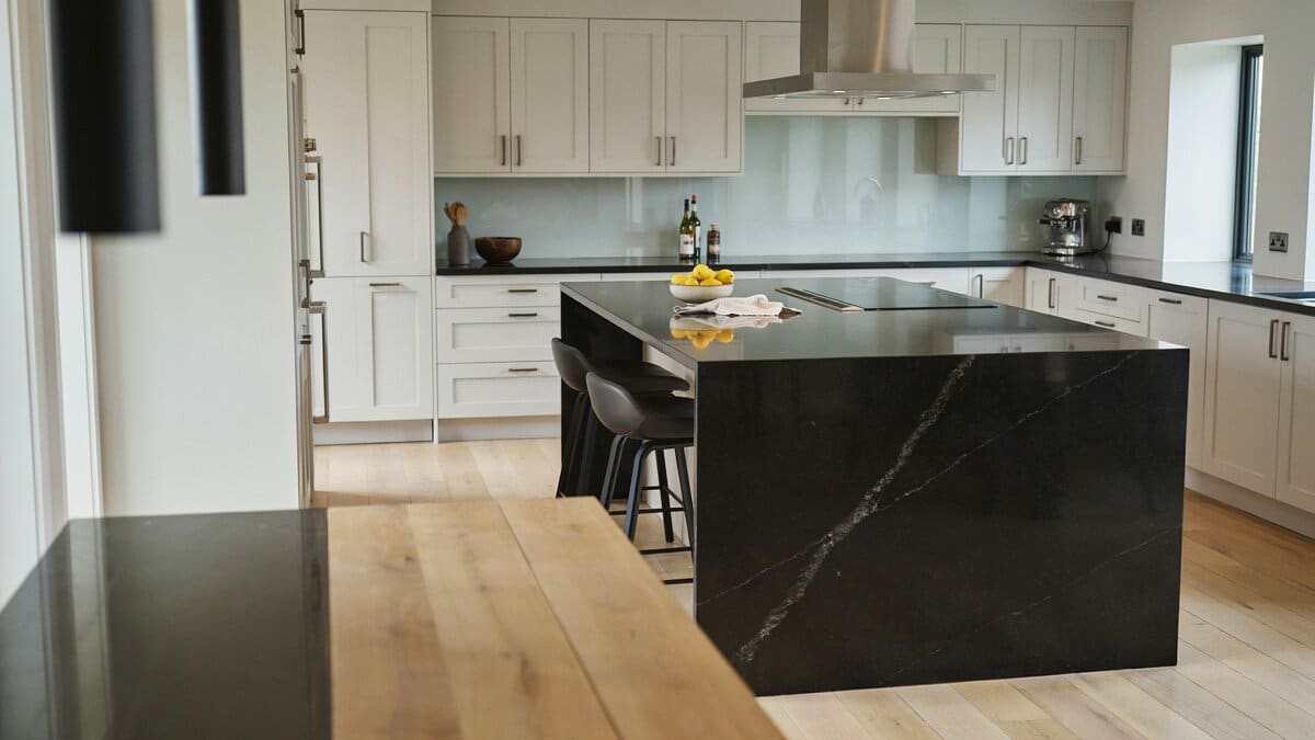 Contemporary kitchen with black granite waterfall island and white glass backsplash