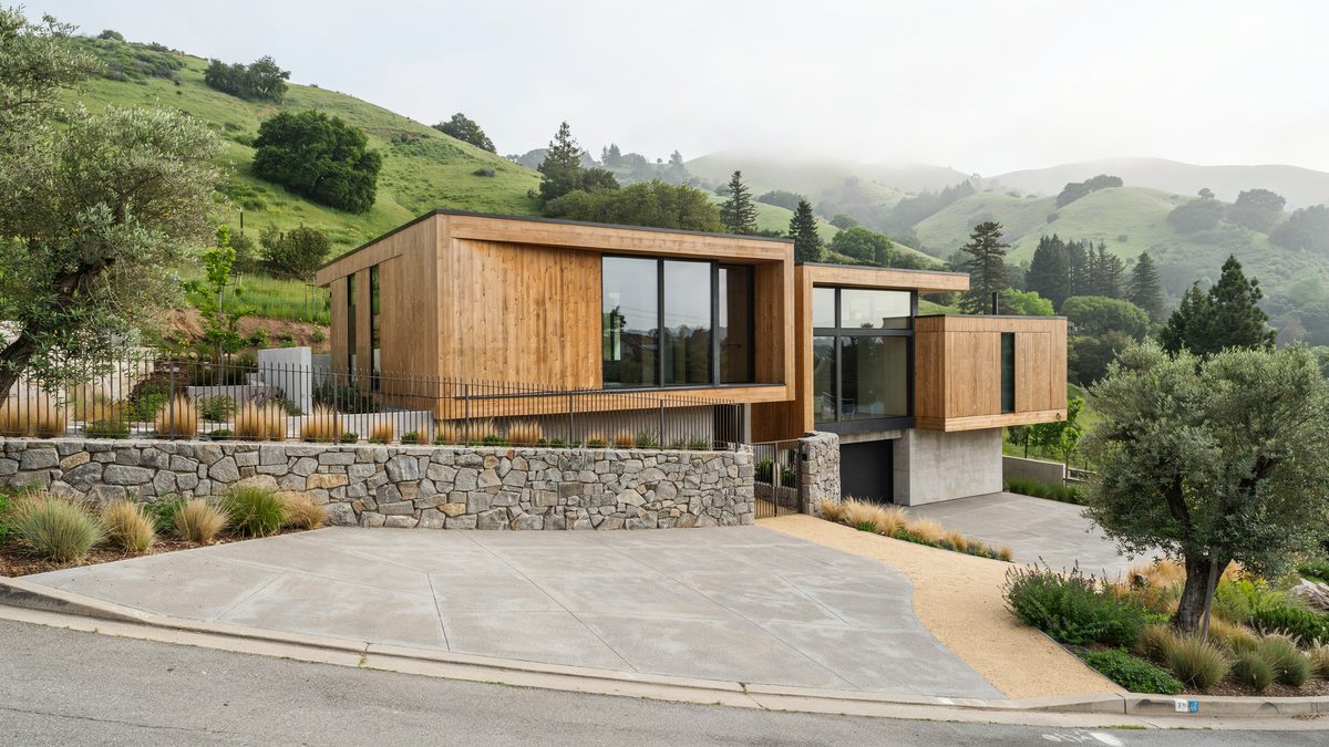 Hillside contemporary home with a stacked stone retaining wall above a wide concrete drive