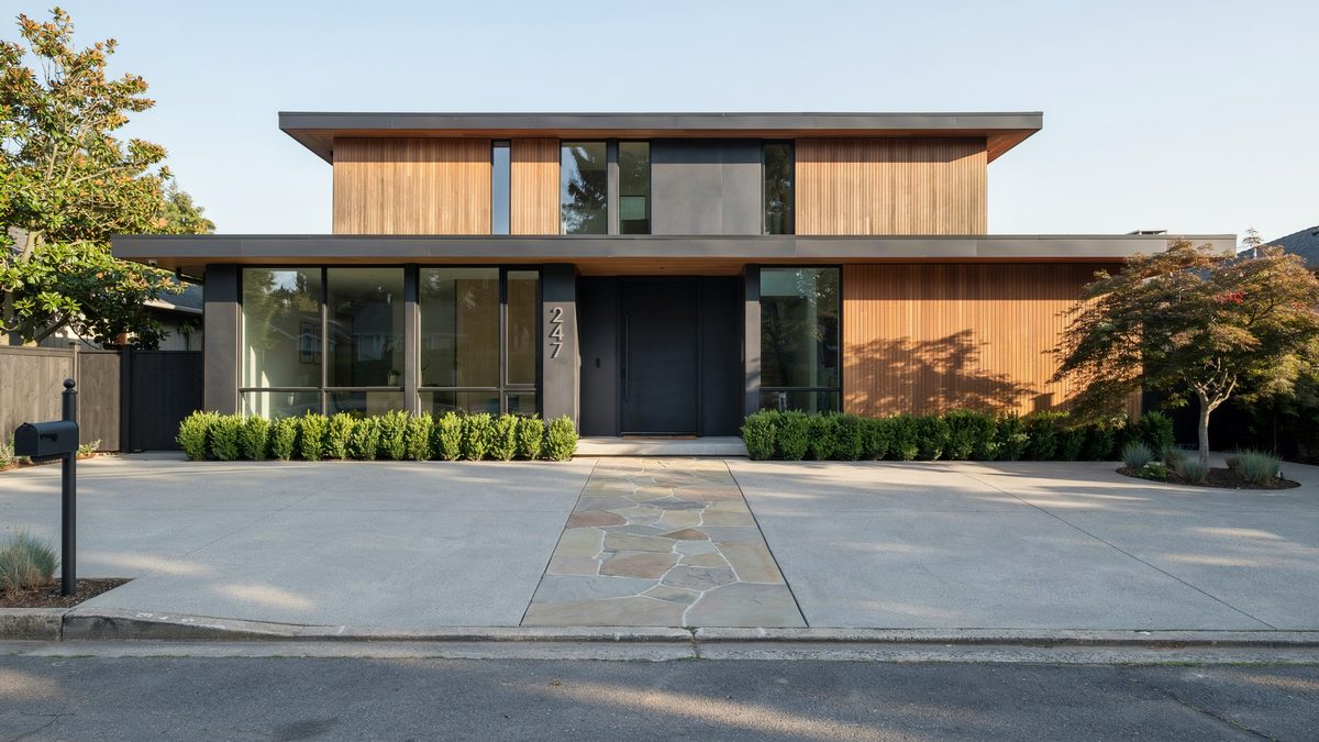 Concrete driveway inset with a band of irregular stone pavers at a wood clad house