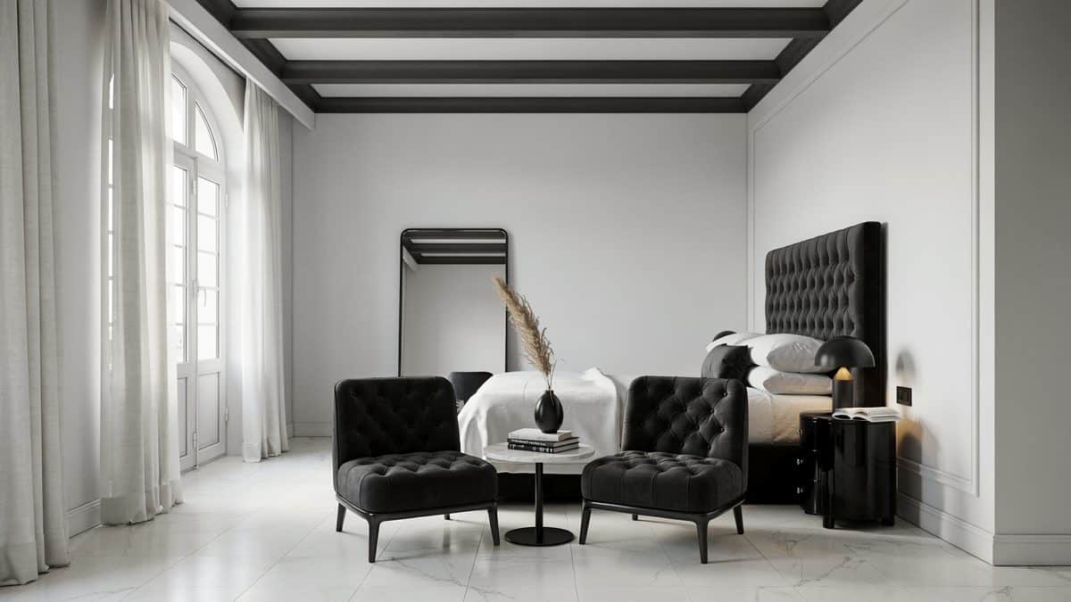 White bedroom with black beamed ceiling, tufted headboard and velvet chairs