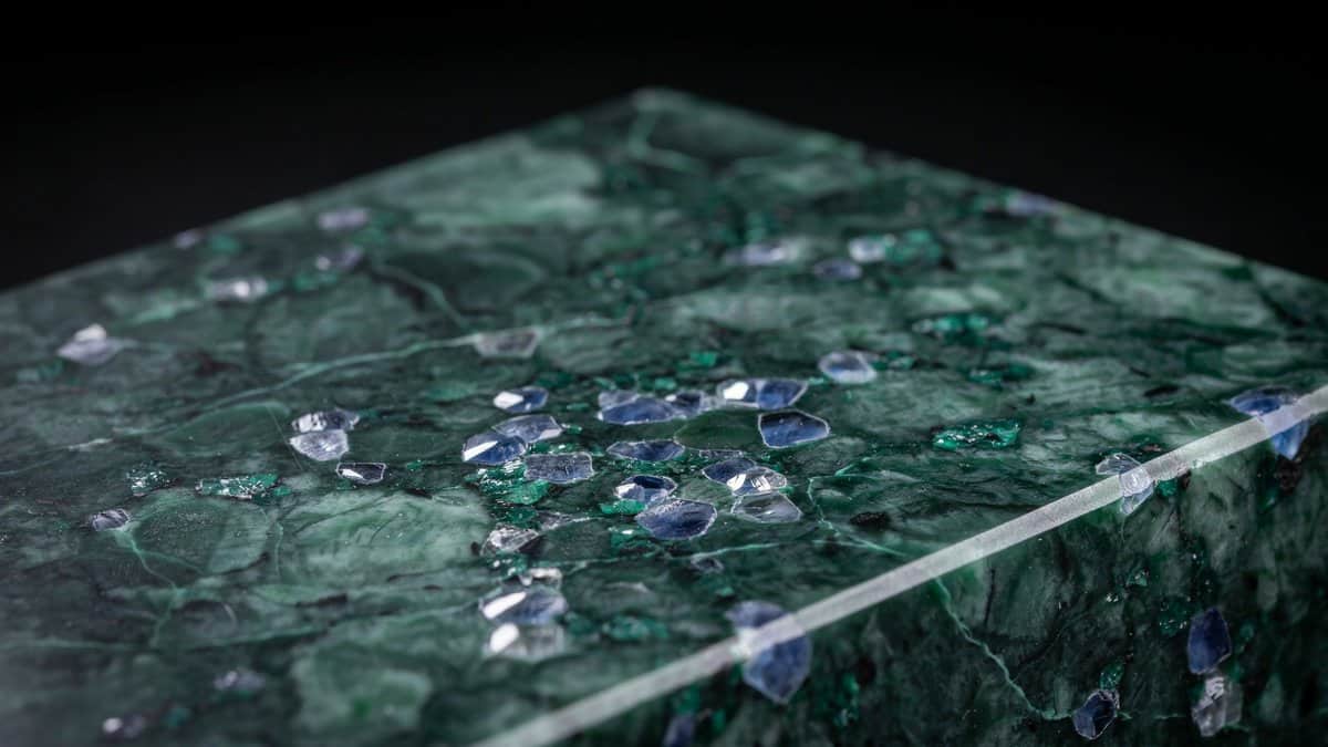 Polished emerald slab edge showing blue crystals scattered across a black base