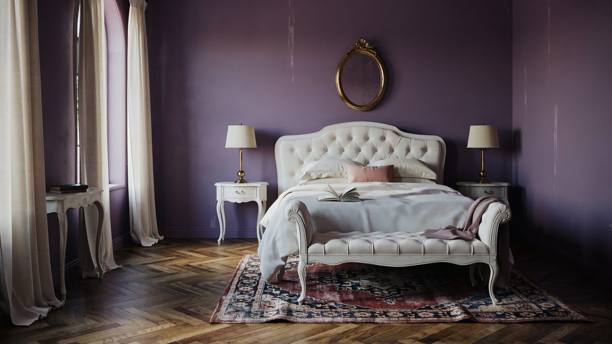 Purple wall bedroom with white tufted daybed and oval gold mirror above