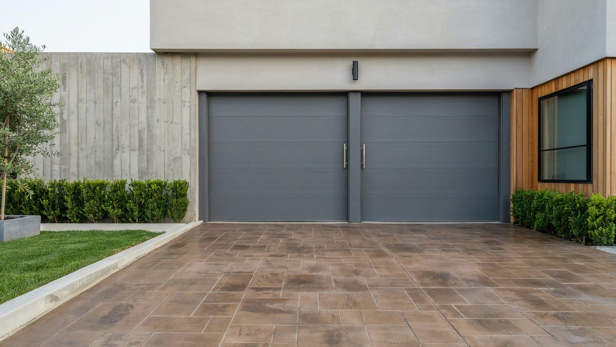 Charcoal double garage doors above a brown concrete paver drive laid in a random pattern