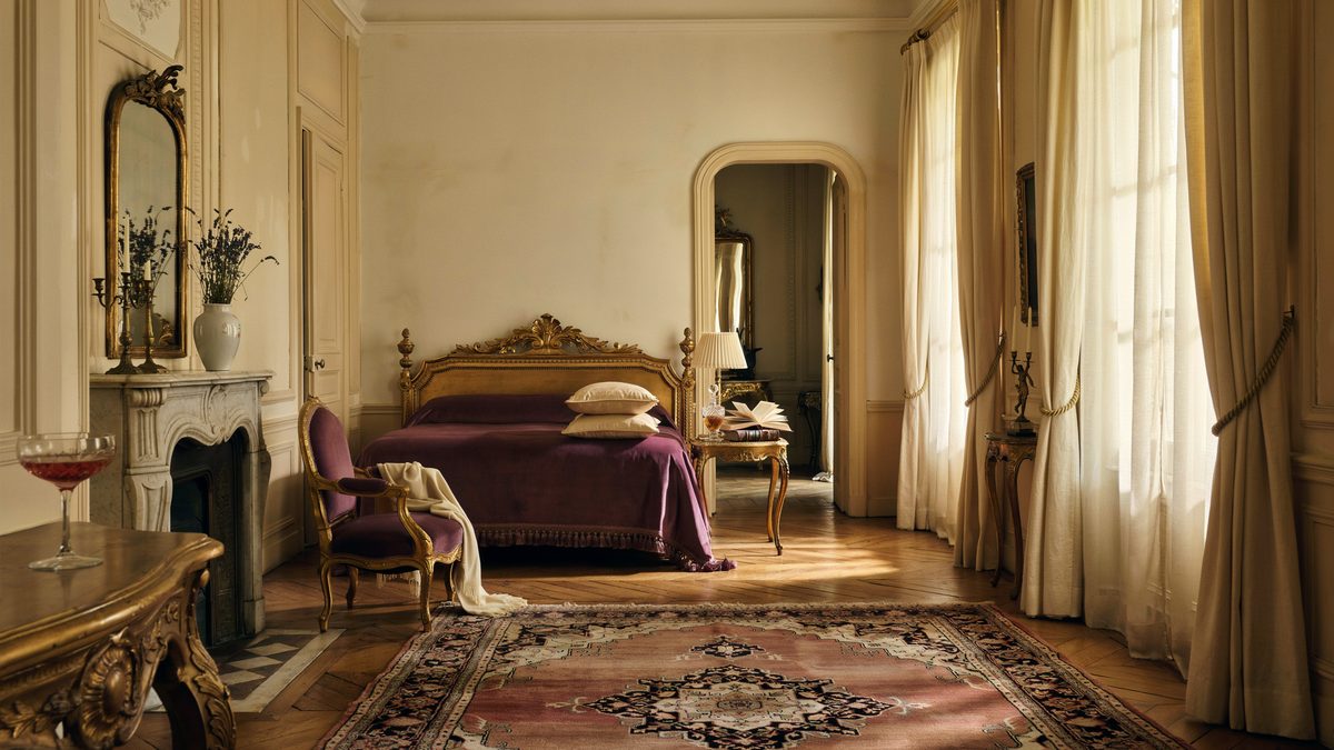 Carved gold bed with plum bedding beside a marble fireplace and gold console